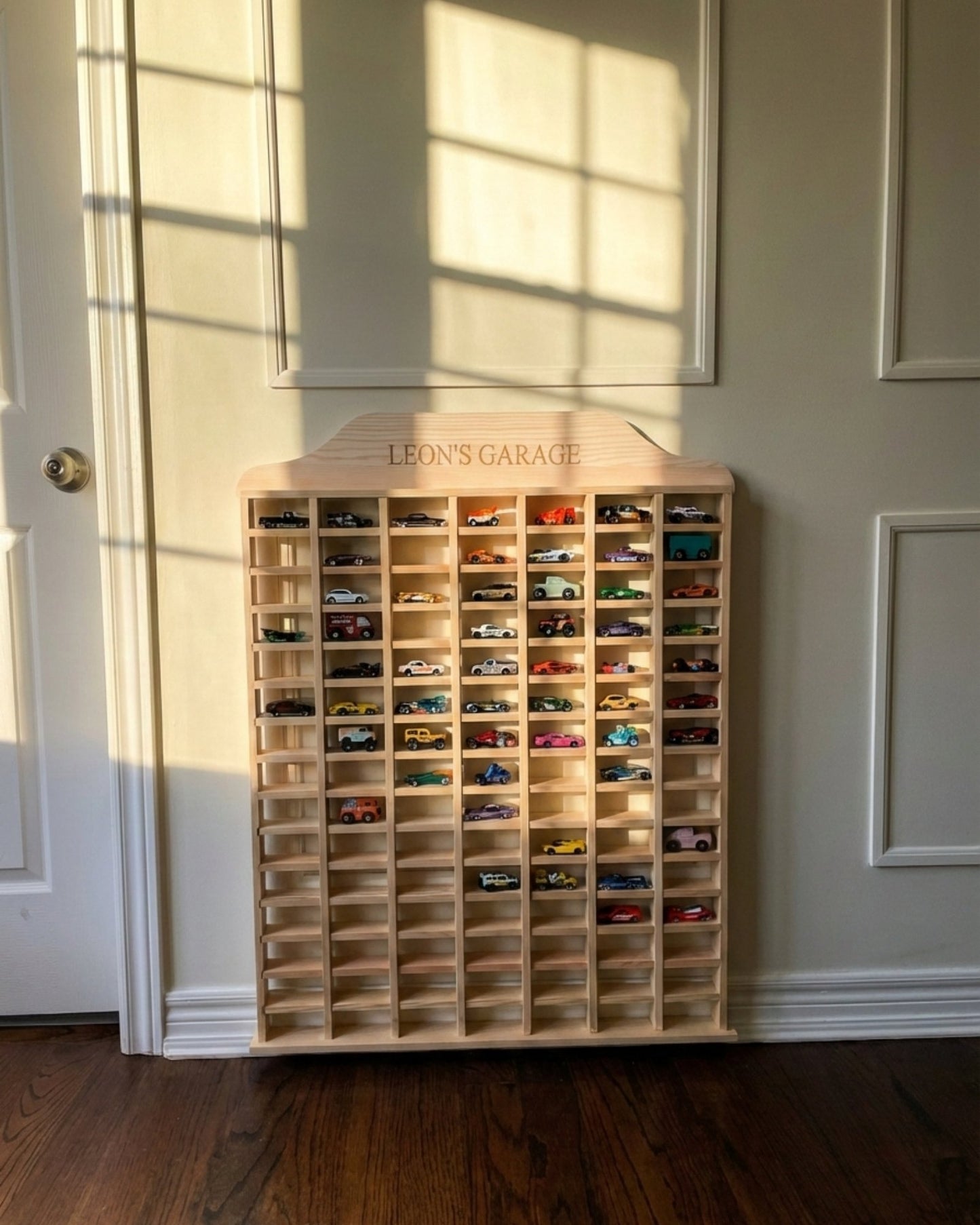 Wooden toy car garage with multiple small cars inside, labeled 'Leon's Garage', against a neutral wall.