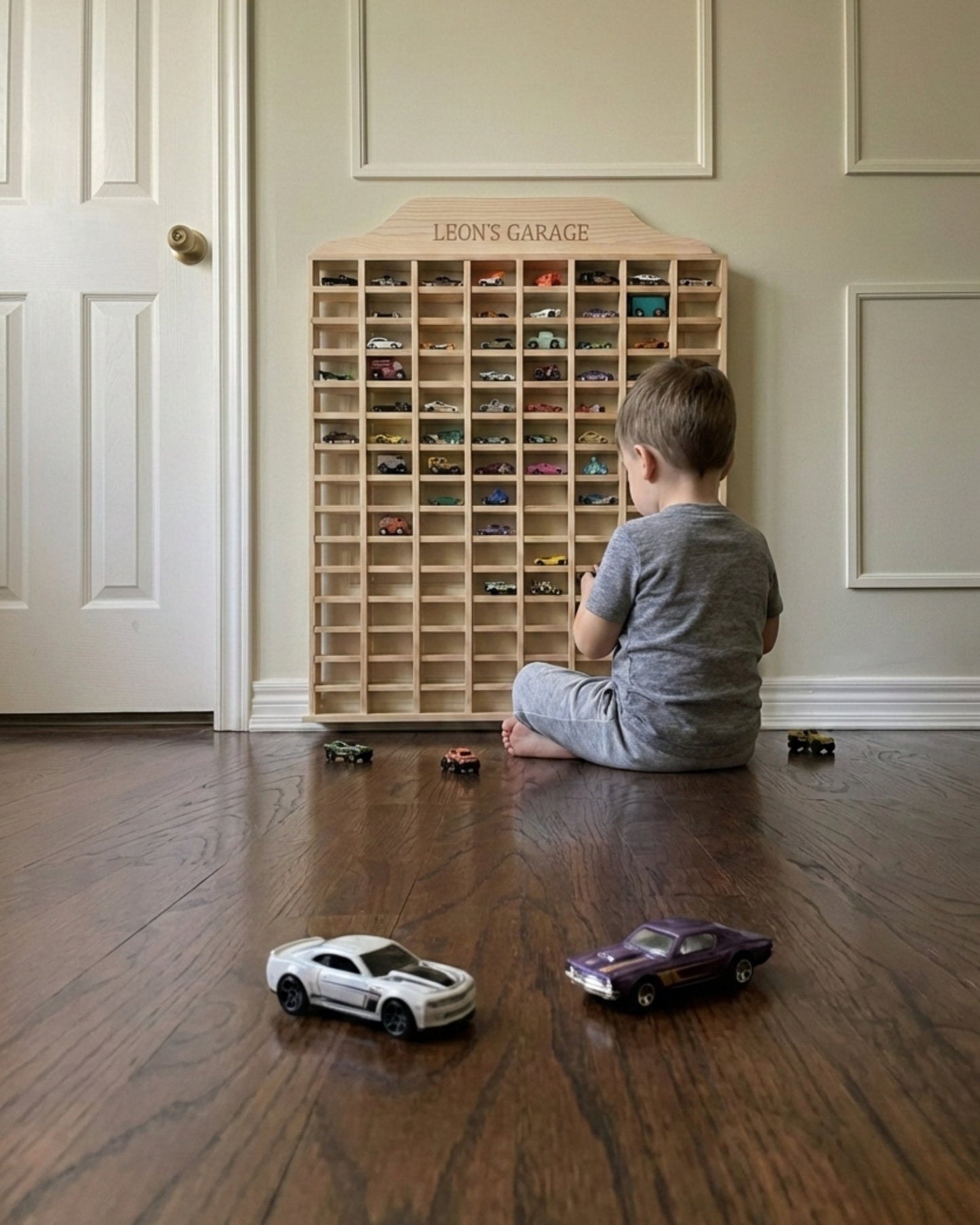 Child playing with toy cars in front of a wooden toy car garage.