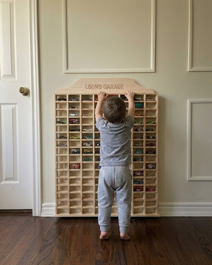 Child playing with a wooden toy car organizer labeled 'Leon's Garage' in a room.