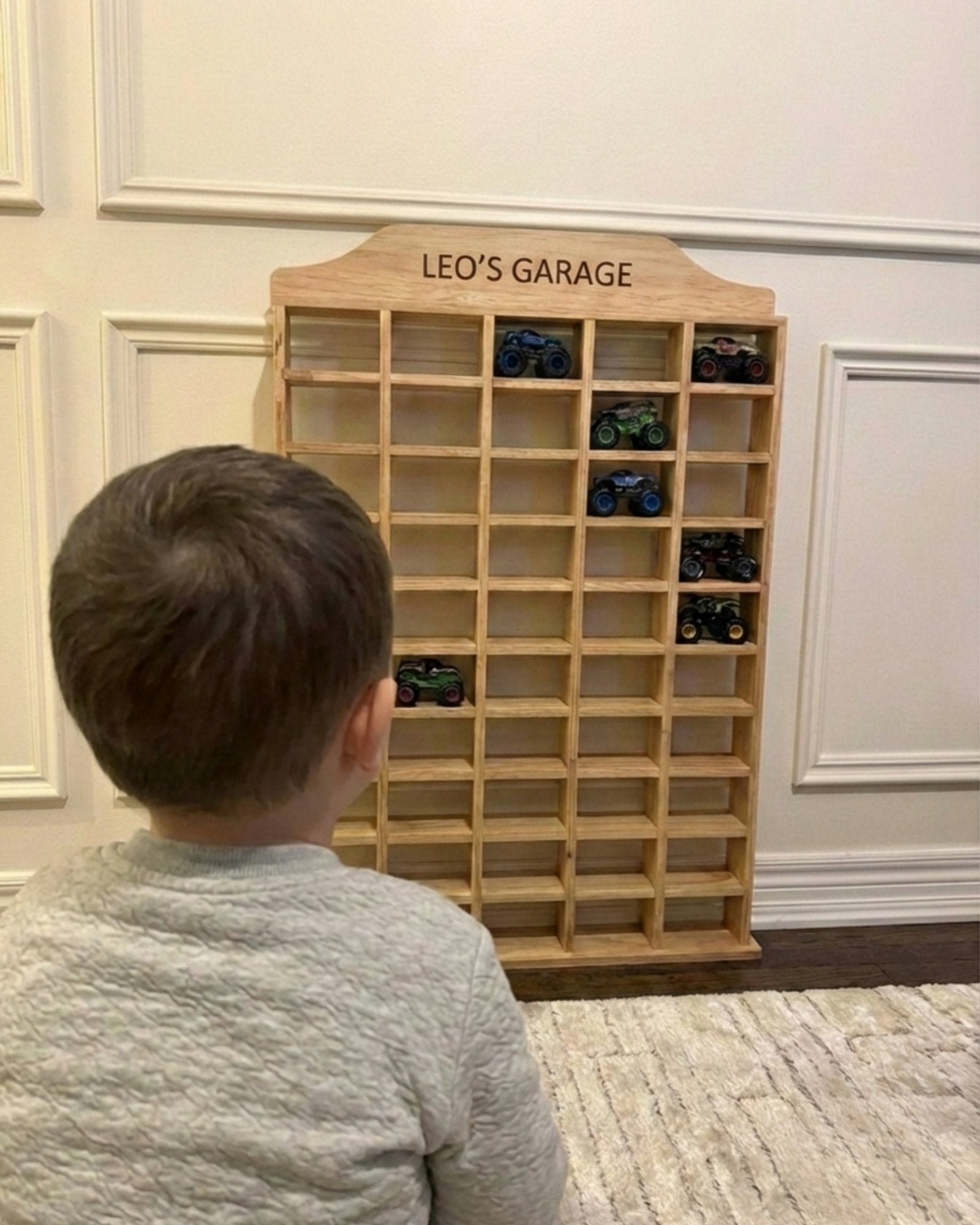 Child looking at a wooden toy car garage with 'Leo's Garage' on top
