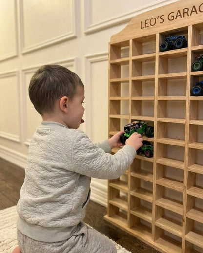 Child playing with toy cars on a wooden shelf labeled 'Leo's Garage'.