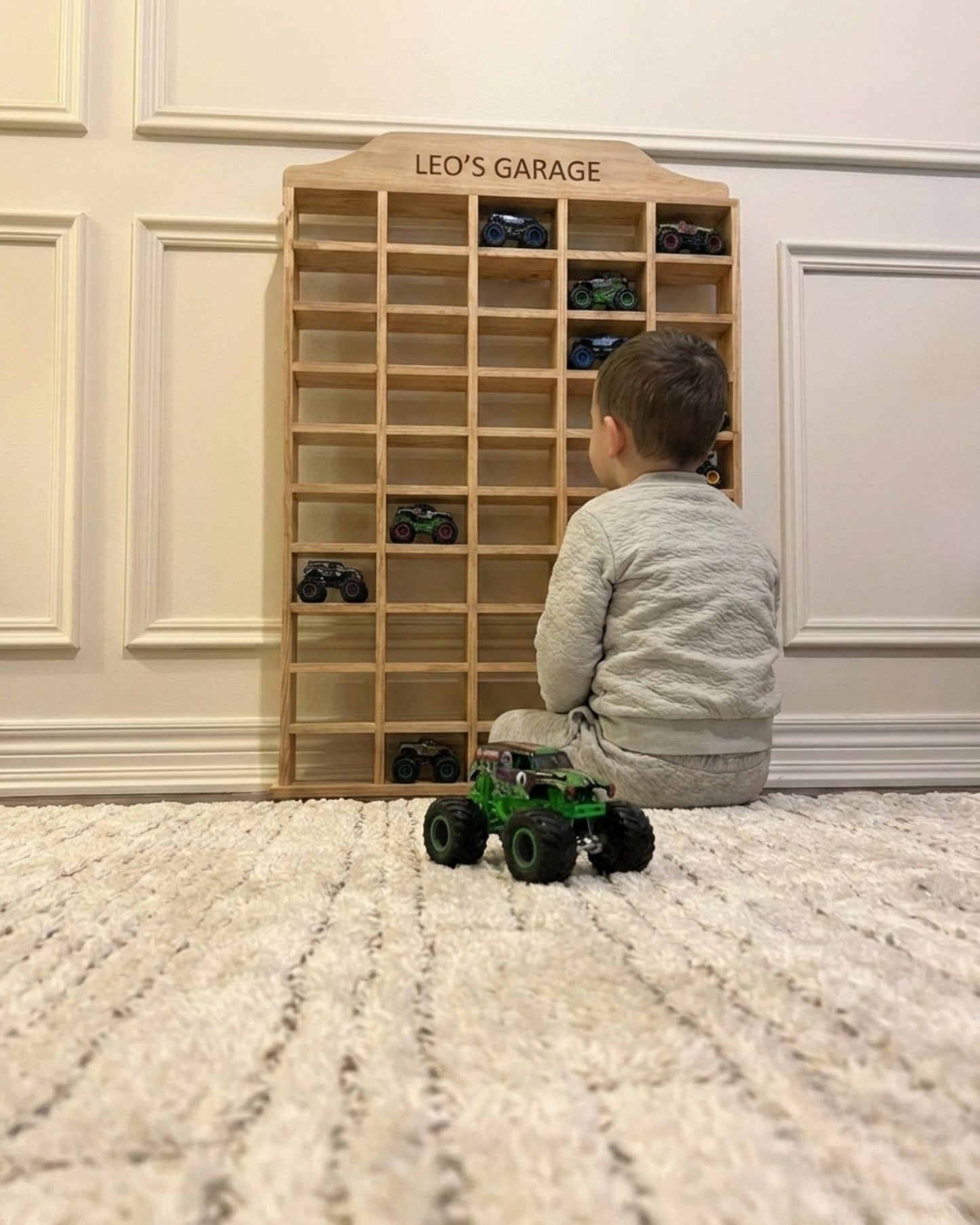 Child playing with toy cars in front of a wooden shelf labeled 'Leo's Garage'.