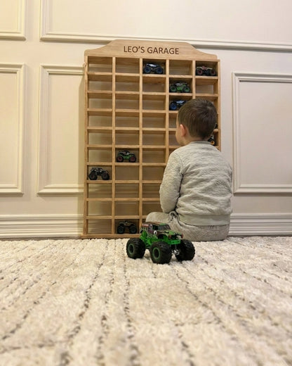 Child playing with toy cars in front of a wooden shelf labeled 'Leo's Garage'.