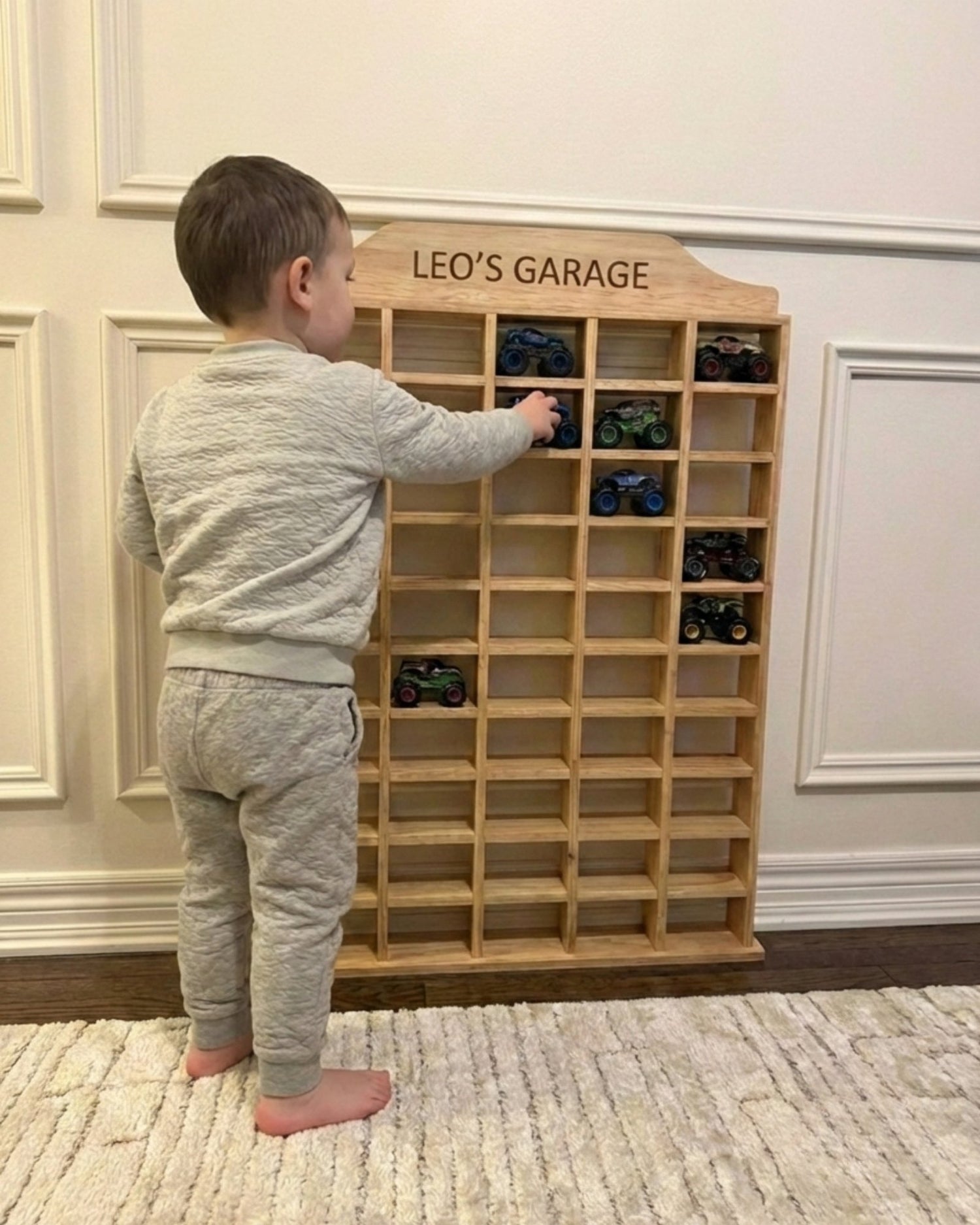 Child playing with a wooden toy car garage labeled 'Leo's Garage' in a room.