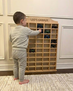 Child playing with a wooden toy car garage labeled 'Leo's Garage' in a room.