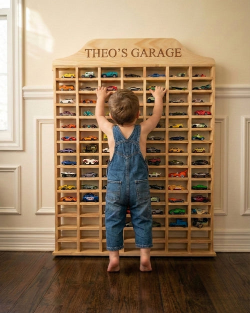 Child in overalls reaching towards a wooden toy car display cabinet named 'Theo's Garage'.