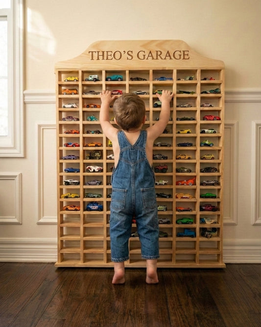 Child in overalls reaching towards a wooden toy car display cabinet named 'Theo's Garage'.