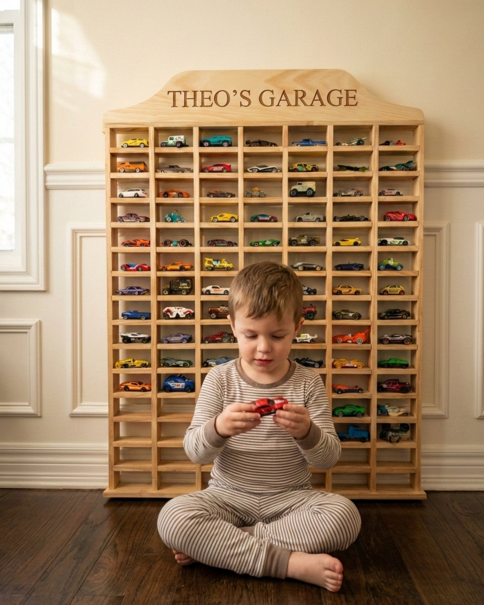 Child playing with toy cars in front of a wooden toy car garage named 'Theo's Garage'.