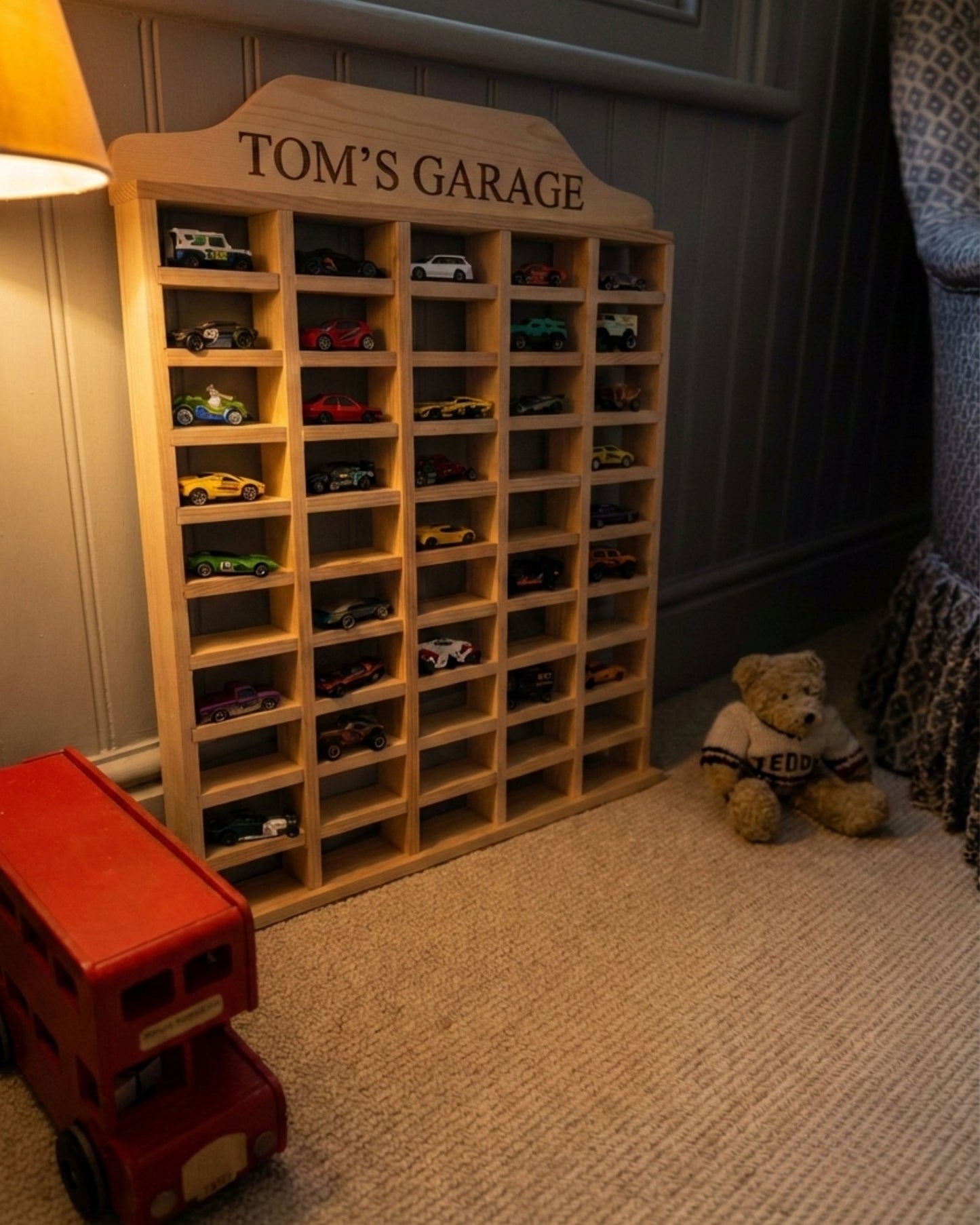 Wooden toy car display with 'Tom's Garage' sign, surrounded by toys on a carpeted floor.