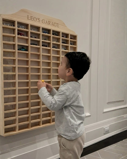 Child playing with a wooden toy car garage labeled 'Leo's Garage' in a room.