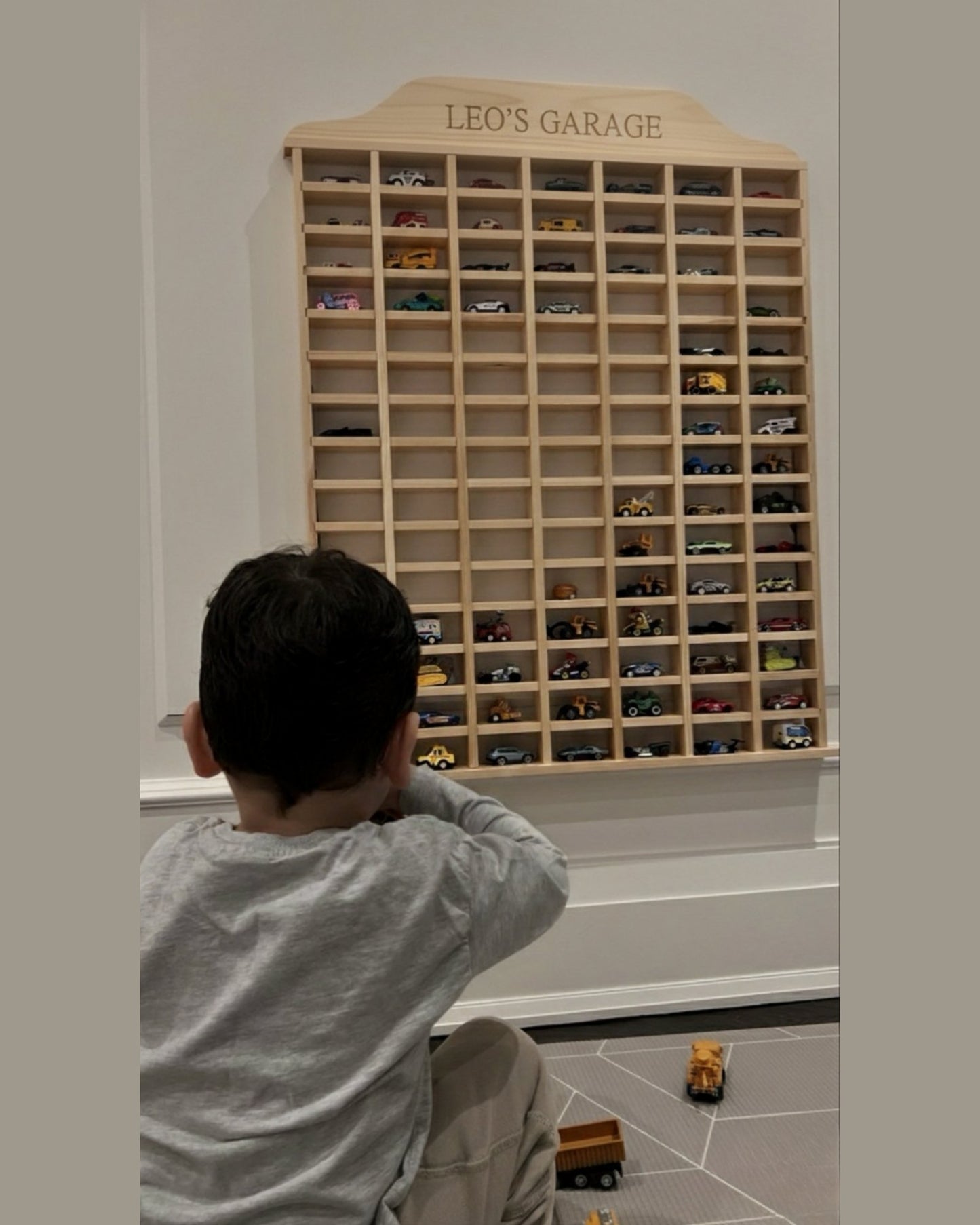 Child looking at a wooden toy car garage with 'Leo's Garage' on top.