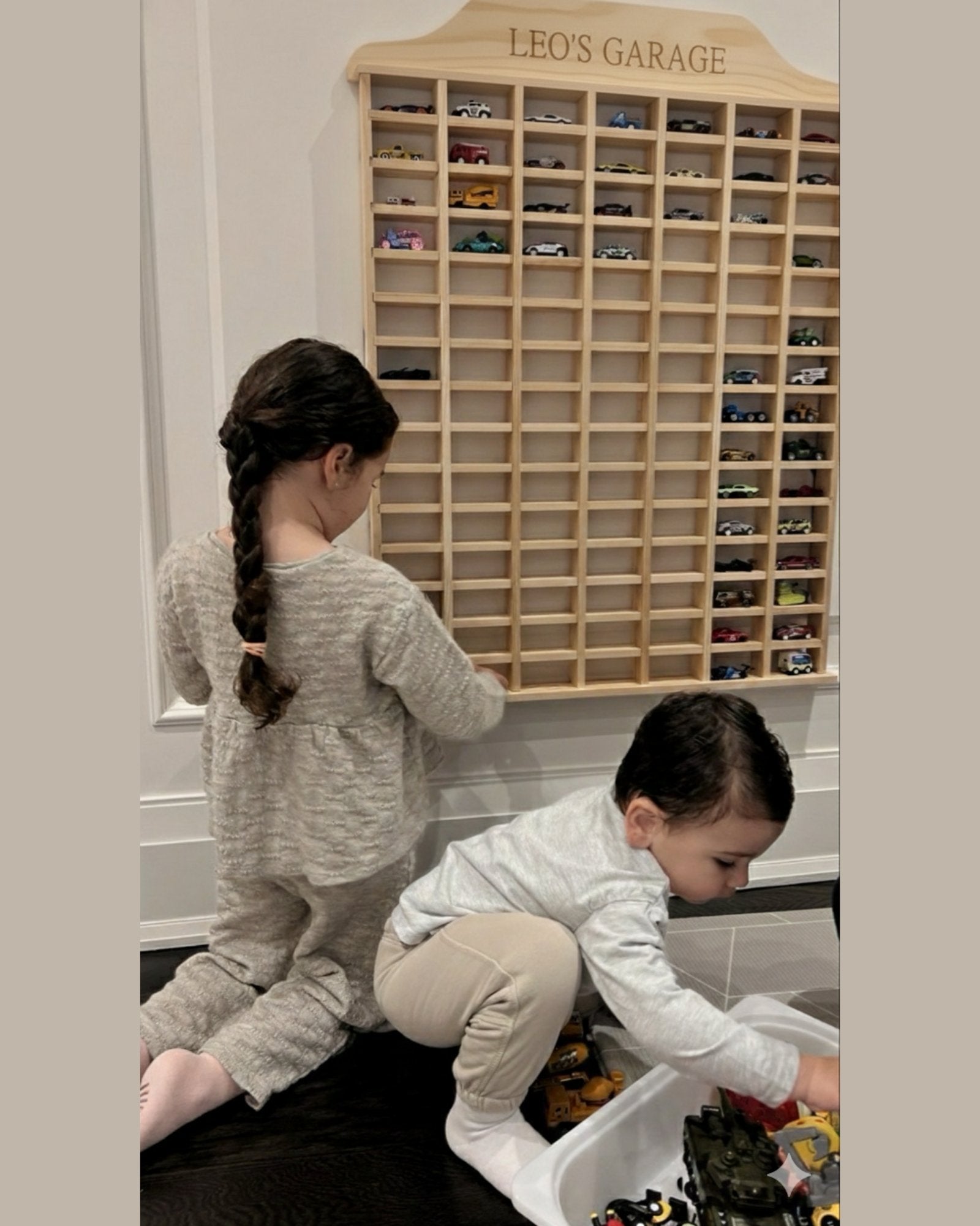 Two children playing with toy cars in front of a wooden toy car garage labeled 'Leo's Garage'.