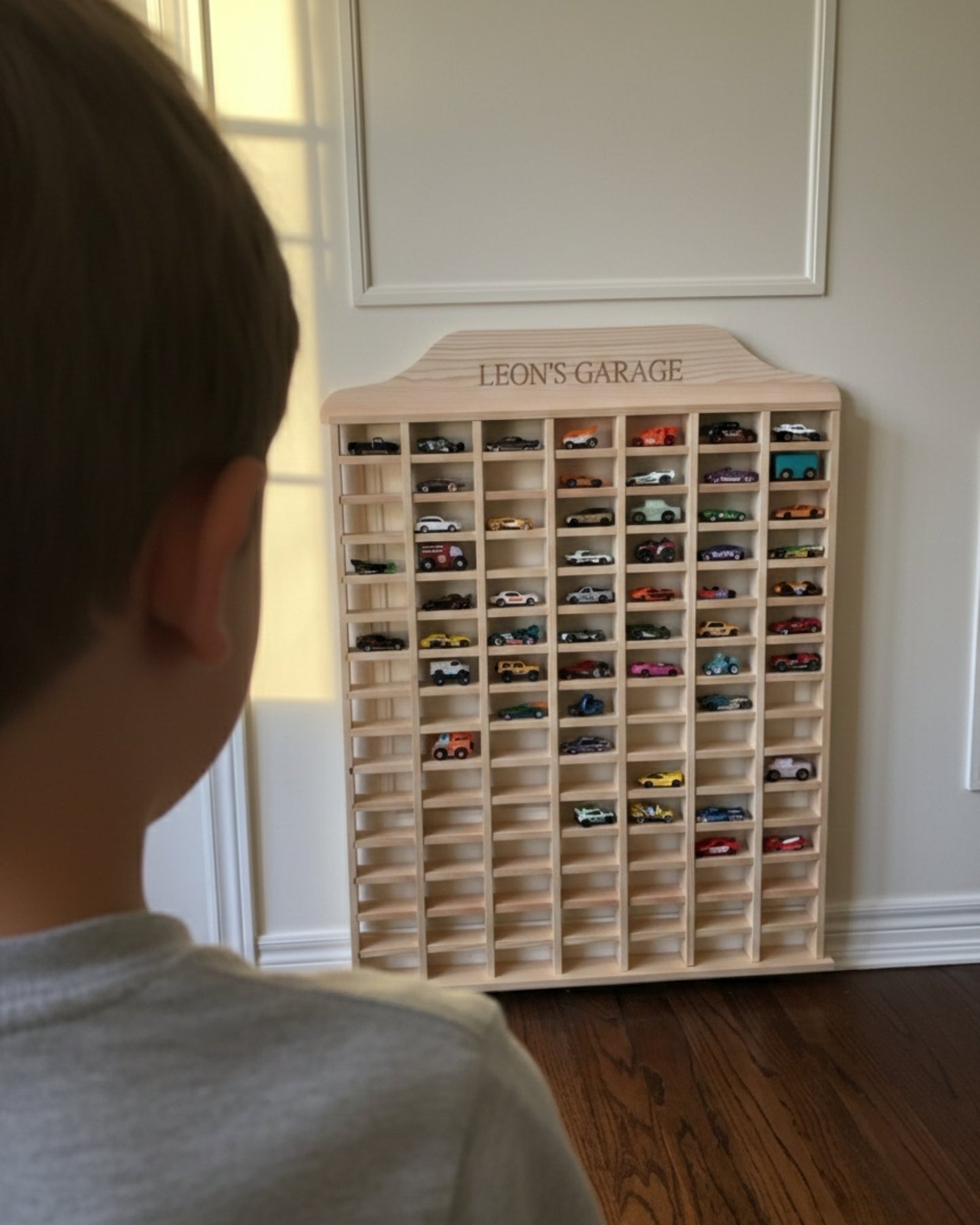 Child looking at a wooden toy car display case labeled 'Leon's Garage' filled with model cars.