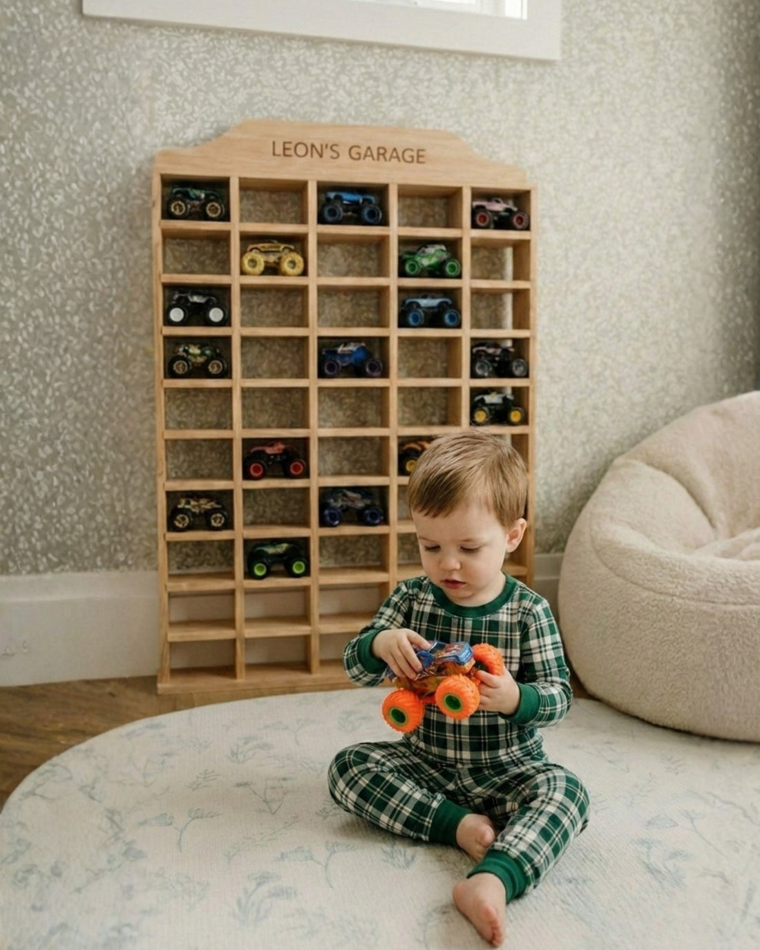 Child playing with toy cars in front of a wooden toy car garage labeled 'Leon's Garage'.