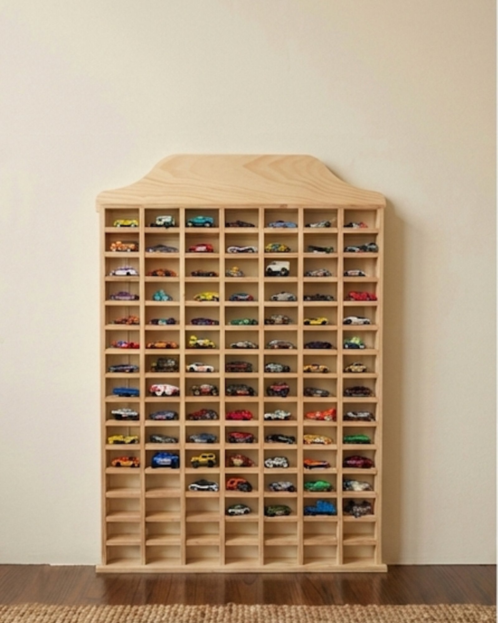 Wooden toy car display case with numerous model cars on a plain wall.