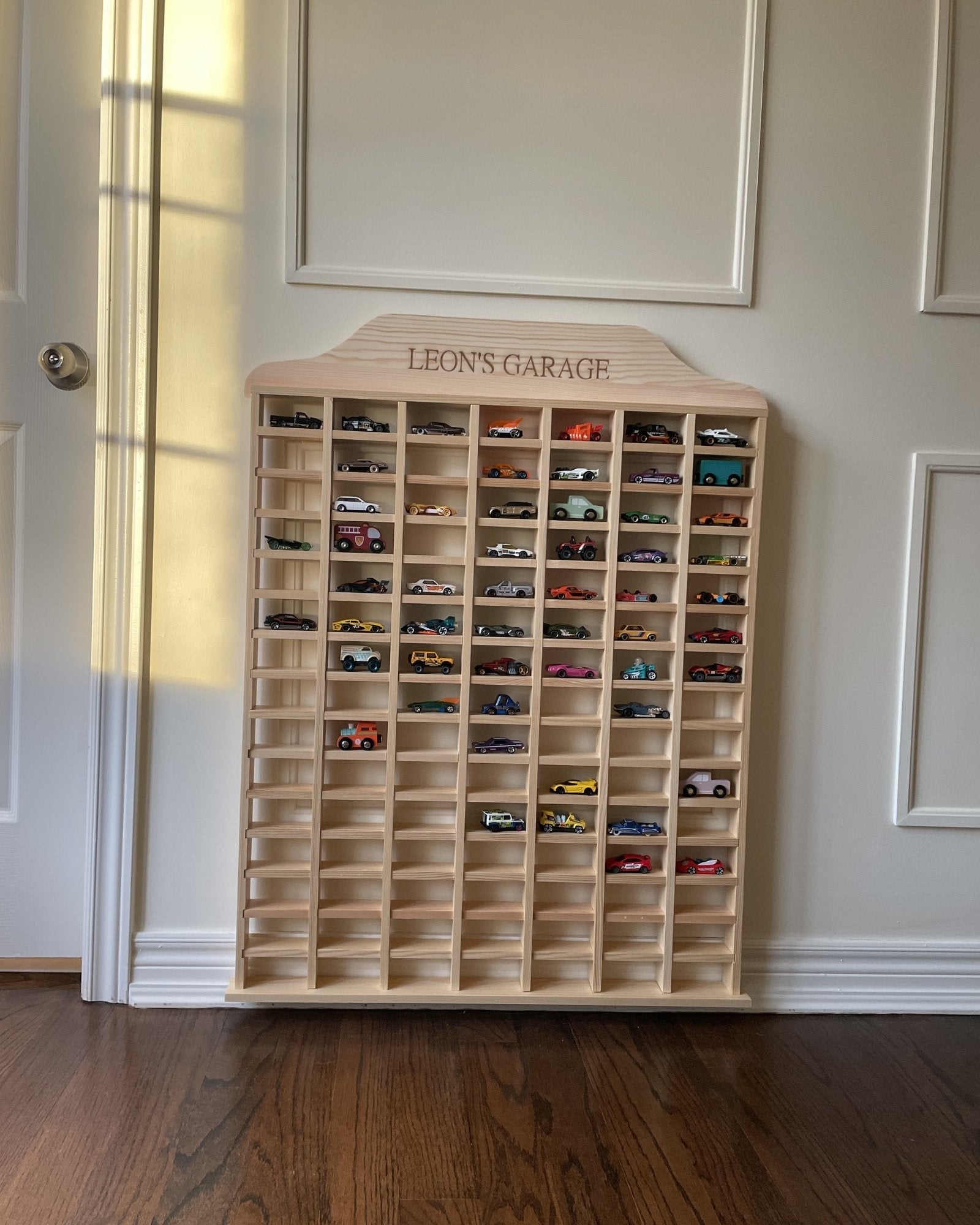 Wooden toy car display case with 'Leon's Garage' branding against a neutral wall.