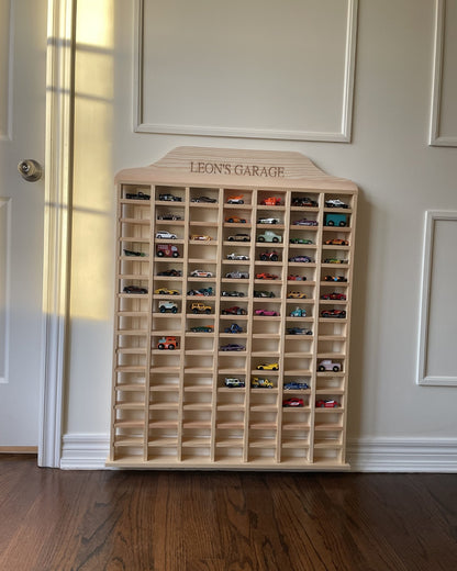 Wooden toy car display case with 'Leon's Garage' branding against a neutral wall.