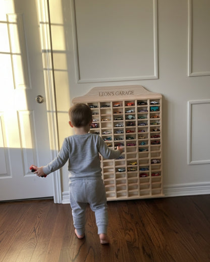 Child playing with toy cars in front of a wooden toy car garage.