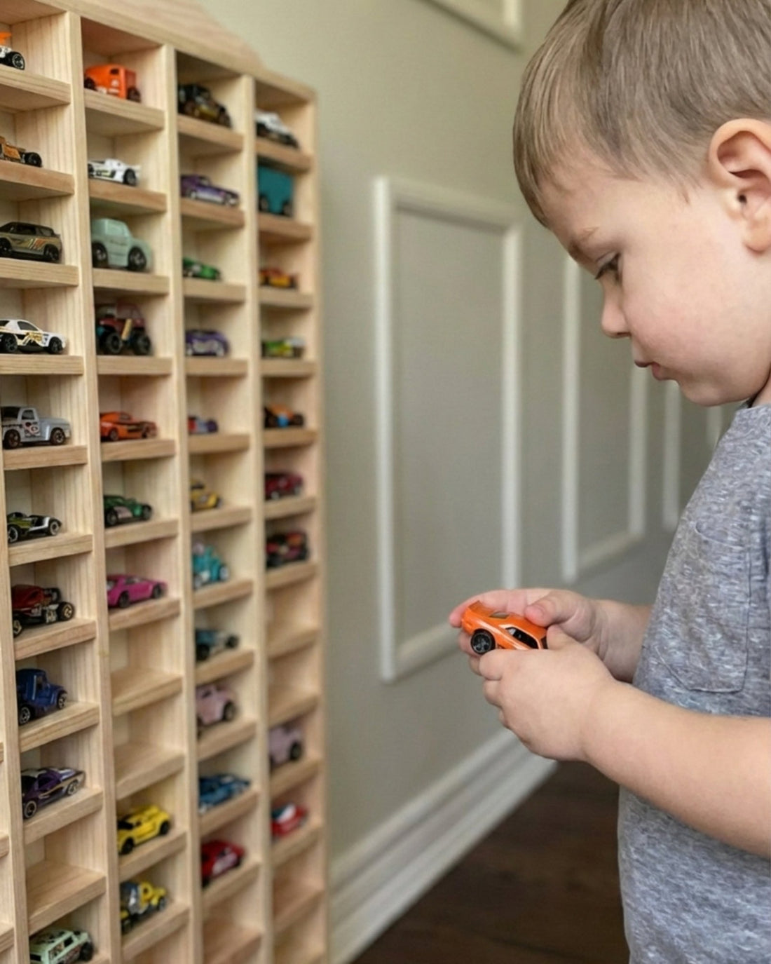 Child playing with toy cars in front of a wooden shelf filled with model cars.