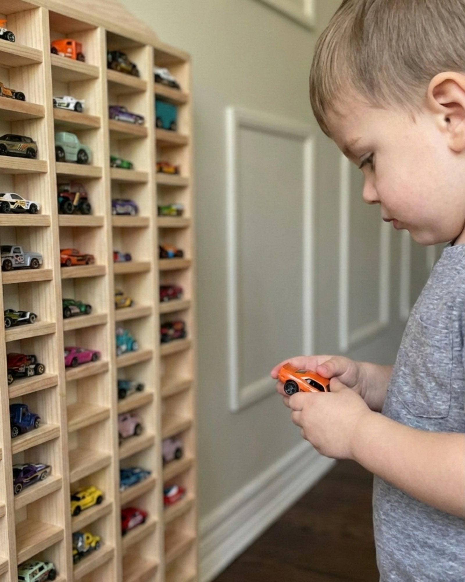 Child playing with toy cars in front of a wooden shelf filled with model cars.
