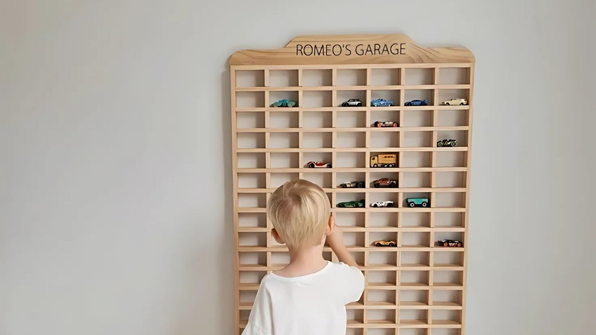 Child organizing Hot Wheels cars in a Montessori-inspired wooden wall display rack for toy storage