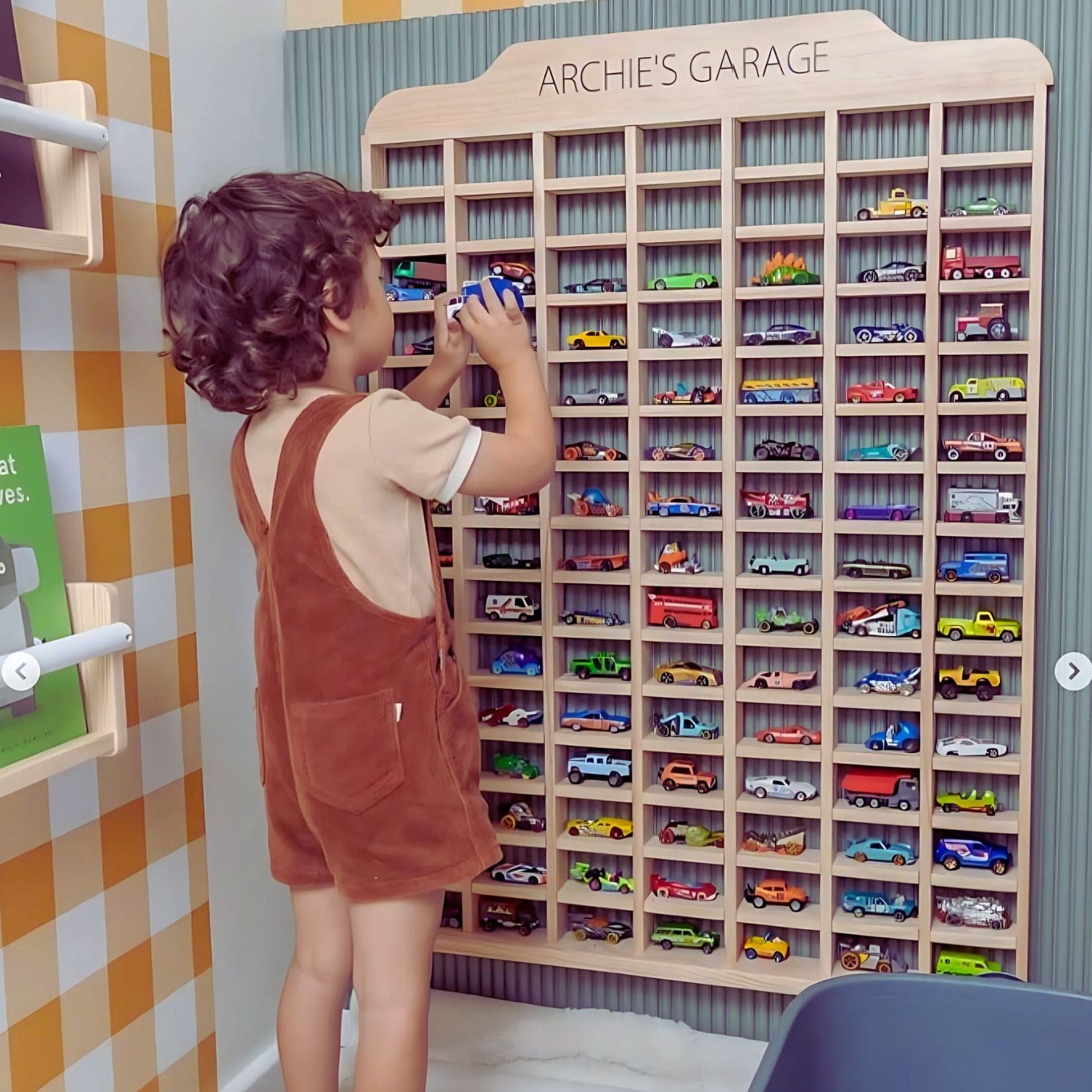 Toddler organizing Hot Wheels cars in a personalized Montessori-style wooden garage display in a playroom